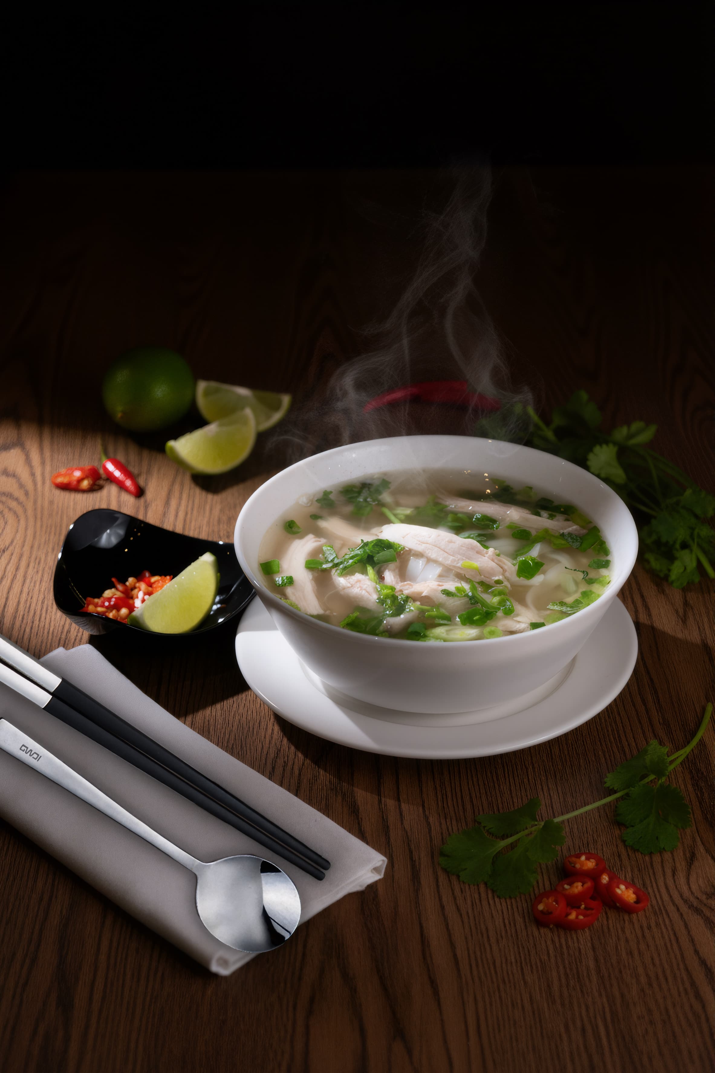 Steaming bowl of chicken pho with lime and chilli