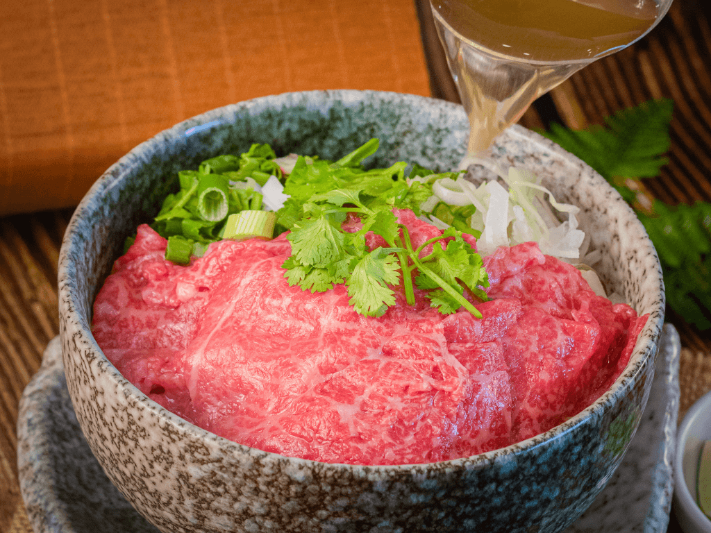 A5 wagyu pho: raw wagyu slices and fresh herbs as hot broth is poured over